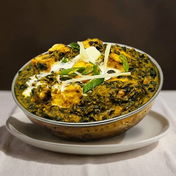 A bowl of vibrant green palak paneer, garnished with cream, ginger, and fresh herbs.