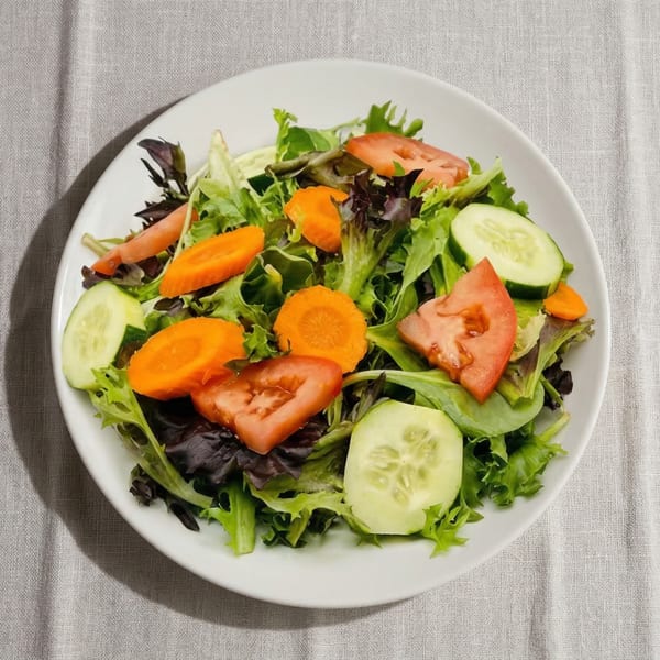 Fresh garden salad with mixed greens, sliced cucumbers, carrots, and tomatoes on a white plate.