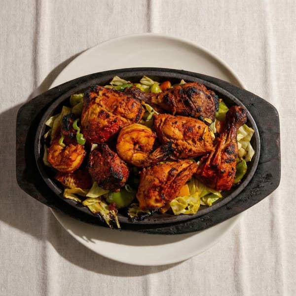 Sizzling platter of tandoori chicken and shrimp with sautéed cabbage and peppers on a white tablecloth.
