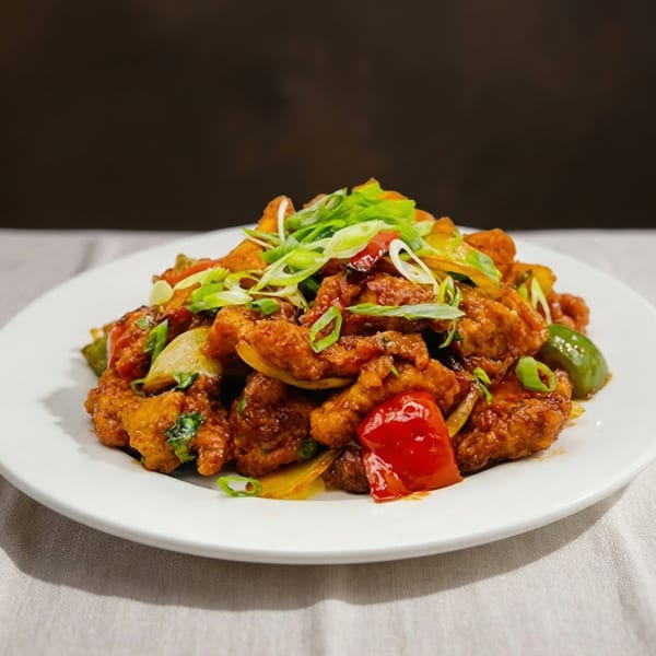 Spicy chicken dish with red and green bell peppers, onions, and scallions on a white plate.