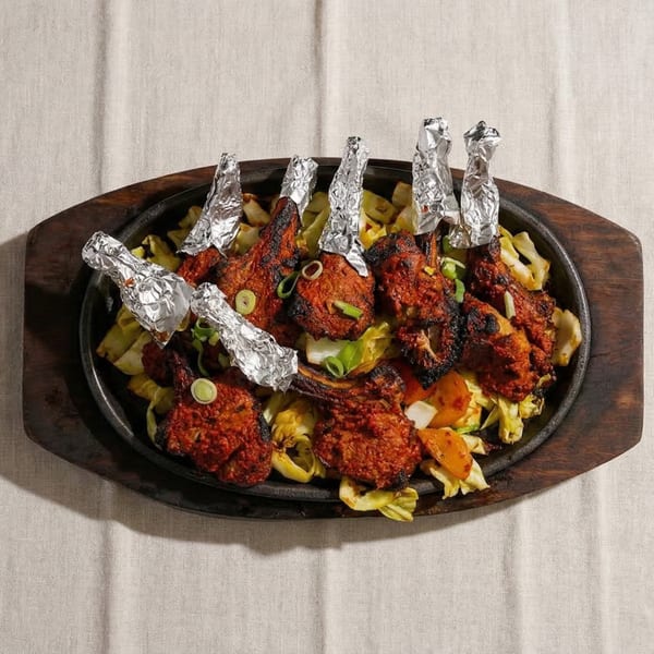 Sizzling lamb chops with foil-wrapped bones, served on a bed of sautéed cabbage and vegetables.